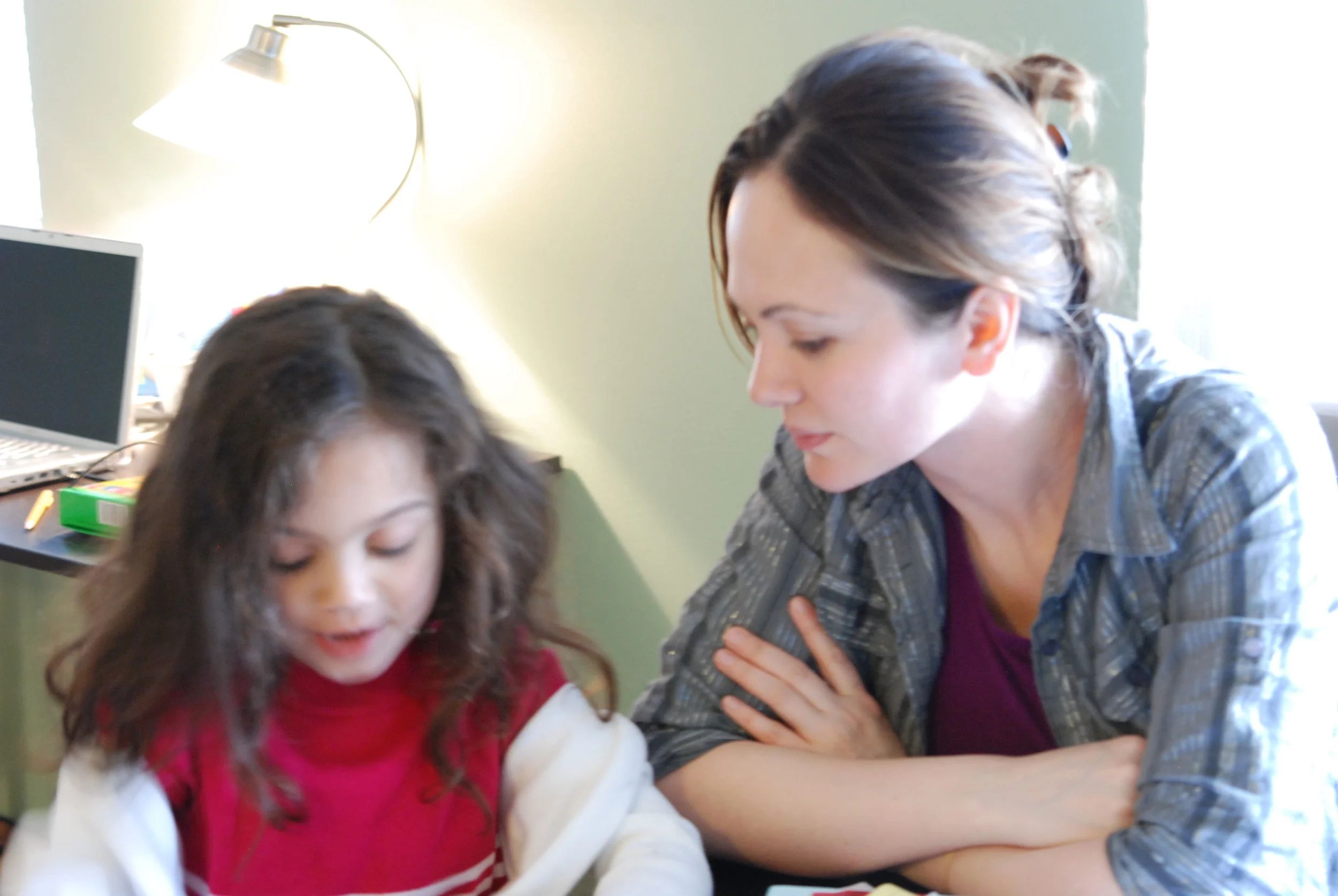 Two women at a desk in a softly lit room, a young girl in the foreground.